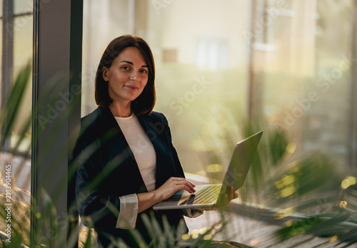 Businesswoman holding an open laptop in a sunlit office