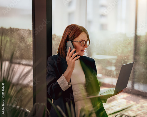 Businesswoman on a phone call working on a laptop by the window