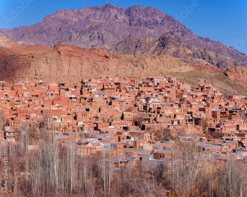 Panoramic view of Abyaneh village, Iran. Traditional red mud-brick houses on a mountainside with rocky peaks in the background. Unique earthen architecture and cultural heritage