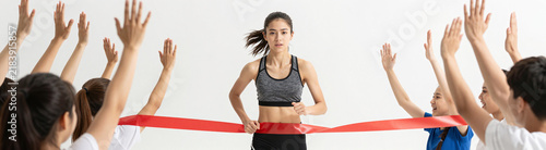 young woman determined expression athletic build wearing running outfit crossing finish line surrounded cheering