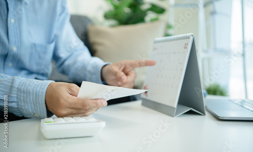 Business professional holding receipts and pointing at calendar for tax deadline planning bill payment scheduling expense tracking budgeting cash flow control and financial management.