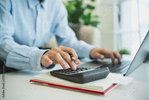 Business professional using calculator and laptop for financial accounting budgeting expense analysis tax planning bookkeeping and efficient digital office management.