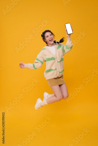 Young woman jumping while showing smartphone blank screen expressing mobile marketing digital promotion social media engagement online communication app advertising and energetic lifestyle.
