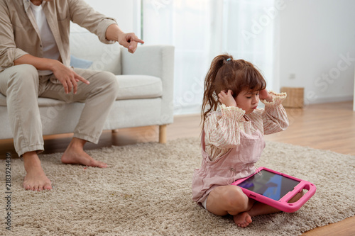 Girl Looks Upset While Using Tablet as Adult Discusses Social Media in Living Room