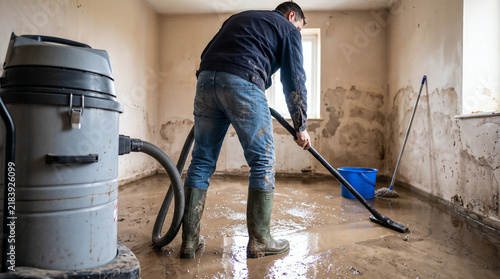 Worker removing flood water with wet vacuum inside damaged home during professional restoration cleanup.