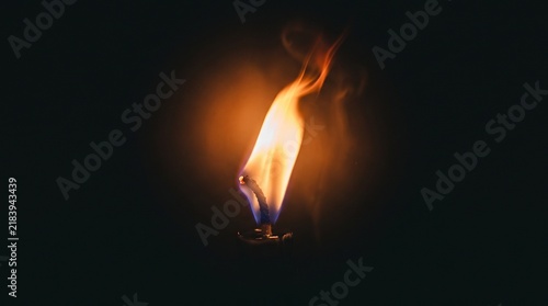 A single glowing orange fire flame burning brightly against a dark black background