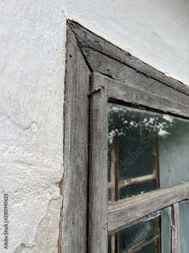 Vertical close up shot of an old weathered wooden window frame on a white stucco wall background