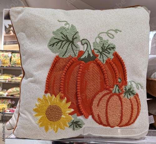 Tiempo de otoño. Cojín con dibujo de calabazas y flor de girasol, con ribete marrón, en estante de tienda de decoración 