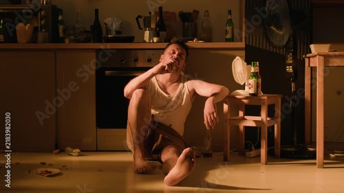 Young adult Caucasian man sitting on kitchen floor suffering from alcohol abuse and intoxication. Useful for substance addiction awareness campaigns and mental health rehabilitation projects