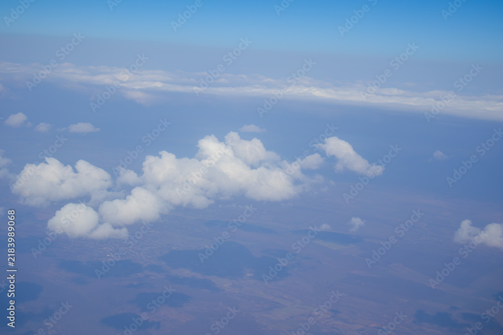 Obraz premium White clouds casting shadows over countryside viewed from an airplane