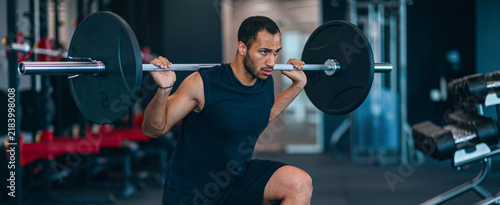 Bild auf Leinwand Focused Black Male Athlete Engaged In Strength Training While Performing Squats With Barbell At Modern Gym