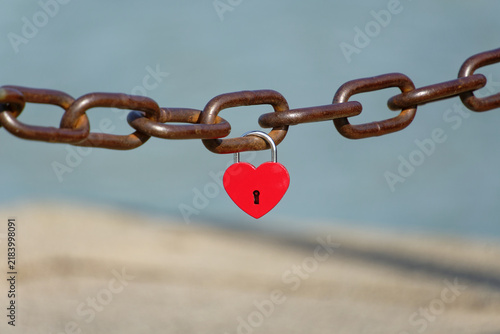Obraz na płótnie Red heart-shaped padlock secured to a rusty metal chain outdoors