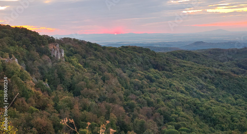 Fotografía The first edge of the rising sun appearing above distant mountain ridges, with Magos-ko visible on the horizon beyond the forested landscape of the Bukk Mountains, Hungary