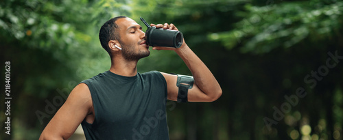 Quadro su tela Focused Black Male Exercising In Outdoor Setting, Enjoying Healthy Refreshment From Mug After Workout