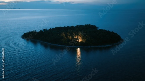 Lonely island with light in trees at twilight over calm water