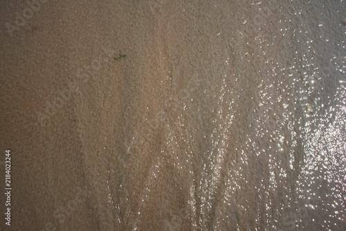 Foto Glinting sunlight on thin layer of water receding over wet sand