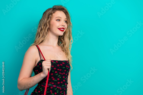 Fotografie Young chic model with cherry print dress smiles against teal blue background for