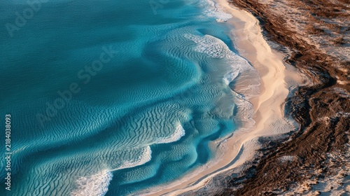 Aerial view of turquoise ocean waves meeting a sandy beach and rocky shoreline