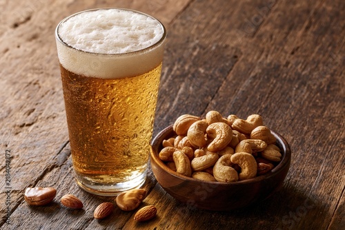 Glass of cold beer with cashews and almonds on wooden table