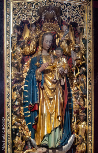 A polychrome wooden statue depicts the Virgin Mary holding child Jesus surrounded by carved angels.