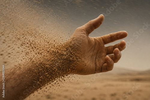 Human hand disperses into blowing sand in a desert scene.