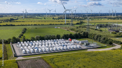 Aerial view of a large-scale battery energy storage system (BESS) surrounded by green fields and wind turbines in rural landscape, renewable energy infrastructure and sustainability concept.