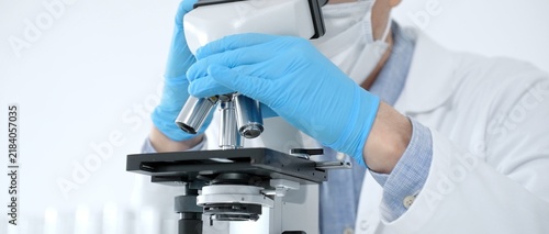 Bild auf Leinwand Scientist in a lab coat and protective gear precisely adjusting a microscope, co