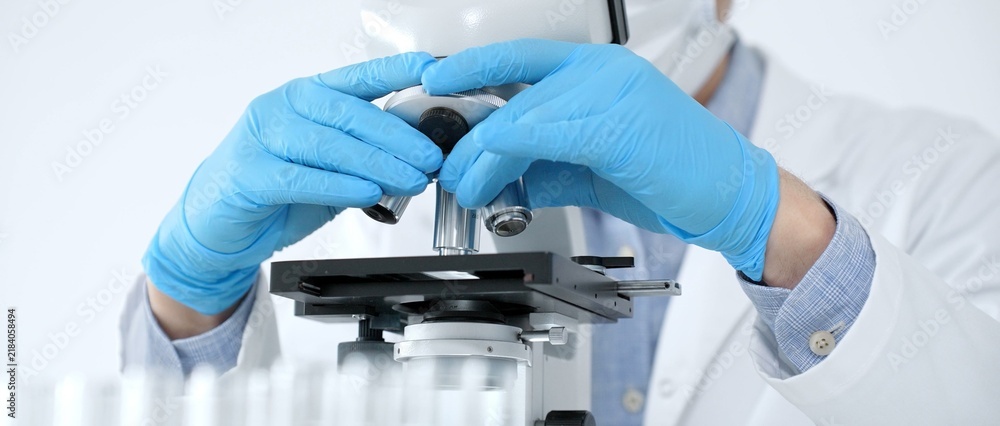 Fotografie Scientist in a lab coat and protective gear precisely adjusting a microscope, co