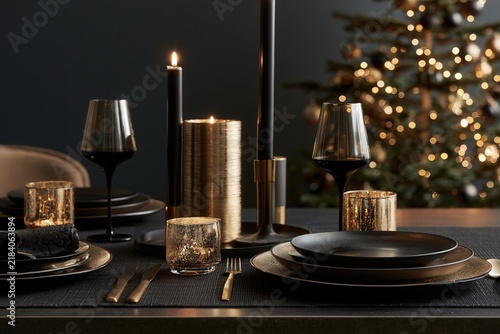 Elegant dark dining table setting with lit candles and Christmas tree in background