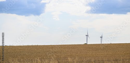 Fotografía Two distant wind turbines rising beyond harvested agricultural field