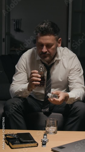 Vertical video of middle aged Caucasian businessman opening decanter and pouring whiskey into glass. Footage represents burnout, work stress, mental health and addiction awareness