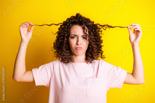 Konstfotografi Frustrated young woman with curly hair pulling strands against a bright yellow b