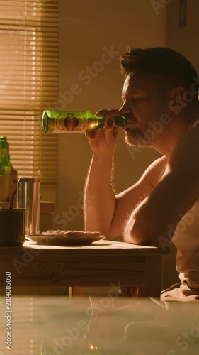 Vertical video of middle aged Caucasian man drinking beer and holding head in despair. Footage suitable for mental health campaigns, addiction recovery, and depression awareness