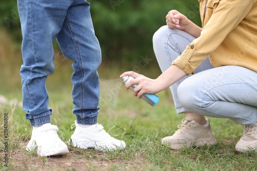 Canvas Print Mother spraying insect repellent onto her son's legs outdoors, closeup