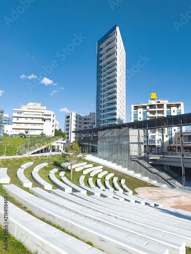 Modern urban park with white amphitheater seating and a tall building in GSP Square. Nicosia, Cyprus