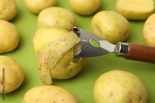 фотографія Ripe young potatoes and peeler on green background, closeup