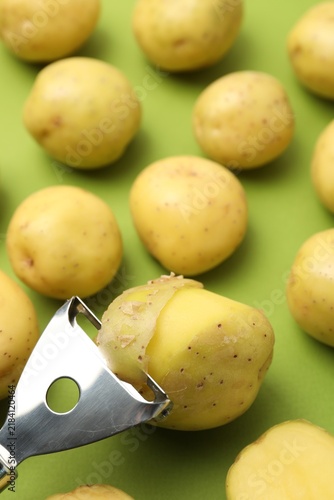 Cuadro en lienzo Ripe young potatoes and peeler on green background, closeup