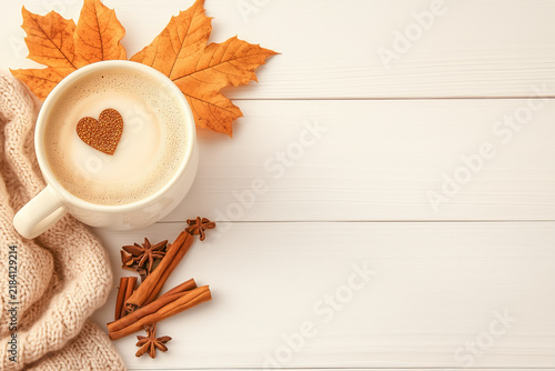 Cozy autumn flatlay with coffee cup, cinnamon sticks, and orange maple leaf on white wooden background.