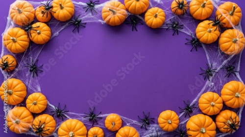 Halloween frame made of small pumpkins and black plastic spiders on a purple background with spider web and copy space