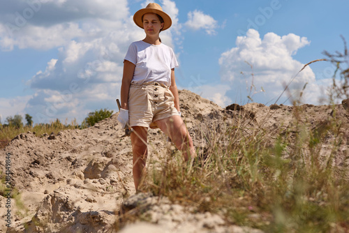 Obraz na plátně An archaeologist stands at a dig site wearing a hat and holding a tool