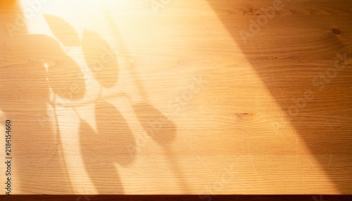 Aesthetic wooden table surface top view with soft overlay shadow of plant leaves. Empty mockup background.