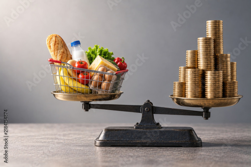 Groceries and stacked coins balance on a vintage scale.