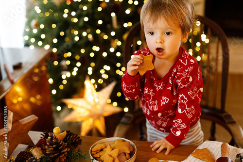 Surprised toddler boy eating star shaped gingerbread cookie at Christmas, concept of holiday wonders, winter treats, festive baking and innocent childhood emotions