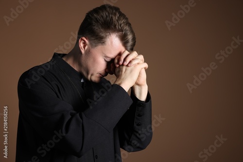 Foto Priest in cassock praying on brown background, space for text