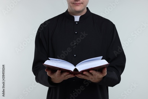 Foto Priest in cassock reading Holy Bible on light background, closeup