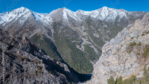 Majestic mountains tower over lush gorges in Kyrgyzstan's Pamir region. Adventure seekers explore the rugged terrain, enjoying the beauty of nature while trekking through picturesque landscapes.