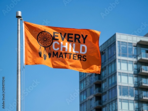 Orange flag with dreamcatcher symbol and every child matters text flies against clear blue sky background