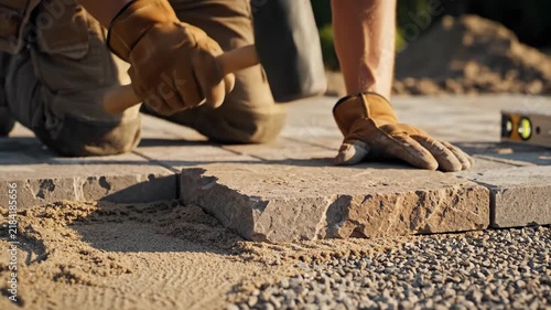 Worker laying paver for patio construction. Hands installing paving stone on sand and gravel base. Home improvement and landscaping project