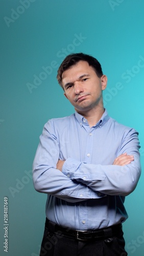 Fotografía Man with folded arms and skeptical expression standing against a clean blue back