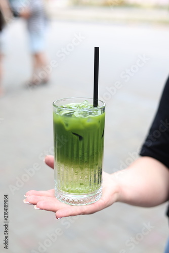 Fotografie Iced matcha tonic cocktail with bubbles in a glass held by woman hand outdoors⁠